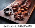 Barbecue spareribs St Louis cut with hot rub and BBQ sauce served as close-up on a wooden cutting board 