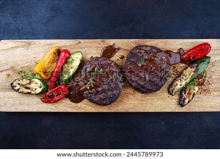 Barbecue wagyu beef Hamburger with grilled vegetable and spicy sauce served as top view on a design wooden cutting board with copy space 