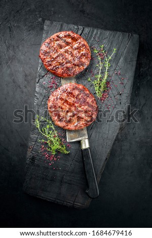 Barbecue Wagyu Hamburger with red wine salt and herbs as top view on a charred wooden board 