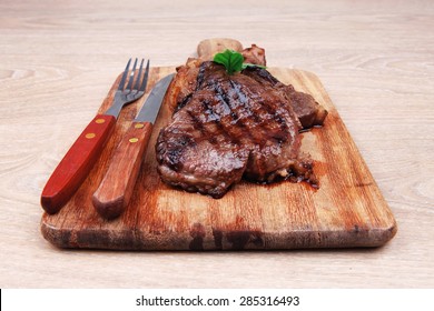 barbecued beef fillet on wooden plate with cutlery over table