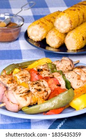 A Barbecued Chicken Kebab Dinner With Corn On The Cob On A Picnic Table Setting.