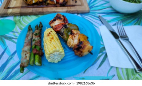 A Barbecued Dinner Of Chicken Kabobs, Corn And Bacon Wrapped Asparagus.