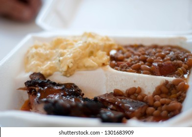 Barbecued Meat With Baked Beans And Potato Salad In A To Go Styrofoam Container