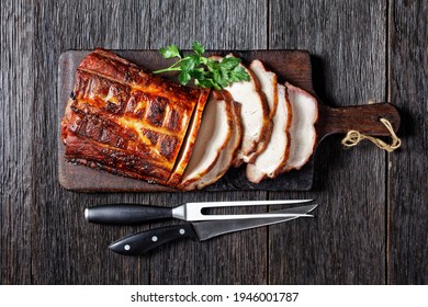 Barbecued Pork Loin Roast Cut On Slices On A Rustic Wooden Cutting Board With Fork And Knife, Horizontal View From Above