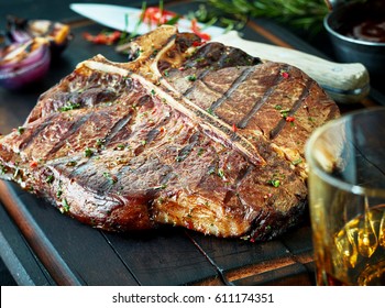 Barbecued t-bone steak seasoned with fresh herbs and marinade served with a glass of whisky or brandy on a cutting board in a steakhouse