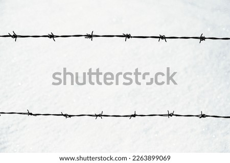 Barbed wire against snow. Rusty metal wire fence. Symbol of concentration camp, prison, jail, borders. 