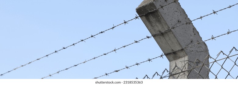 Barbed wire and blue sky in background. Concrete fence post and prison