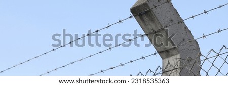 Barbed wire and blue sky in background. Concrete fence post and prison