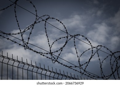 Barbed wire fence in dark colors on background with dark sky. Metaphor concept of prison, jail, arrest. Prohibbited zone and area