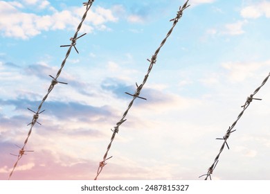 Barbed Wire Fence Silhouetted Against Cloudy Sky at Sunset - Powered by Shutterstock