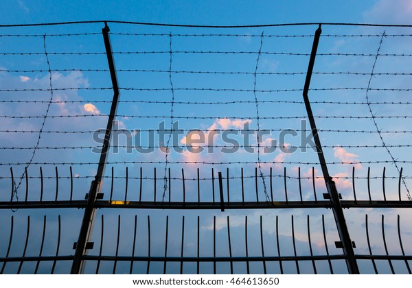Barbed wire fence silhouettes against cloudy dark\
blue sky at sunset