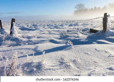 Barbed wire fence with snow covered ground and fog