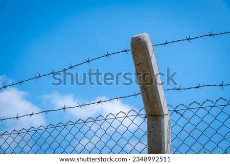 barbed wire, metal mesh wire and concrete pole. blue sky background.