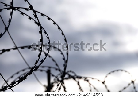 Barbed wire on background of dramatic sky with clouds. Concept of boundary, prison, war or immigration