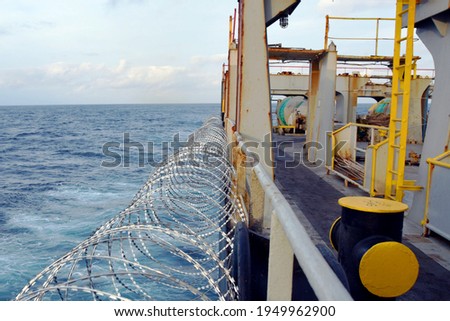 Barbed wire or razor wire attached to the ship hull, superstructure and railings to protect the crew against piracy attack passing Gulf of Guinea in West Africa.
