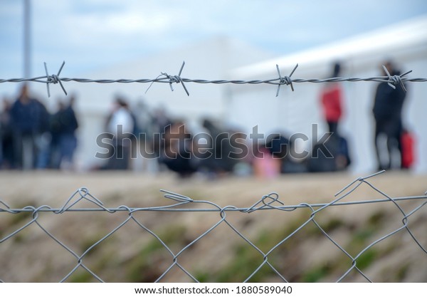 Barbed wire in refugee camp. Migrants behind chain\
link fence in camp. Group of people behind fence. Concept of\
prison, freedom, barrier, security and migration. Refugees on their\
way to EU.