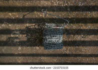 Barbed wire and steel handle on a ground. A metal nest with a metal fence for carrying objects. The concept of guarding the territory. Protection from insects and barbwire.