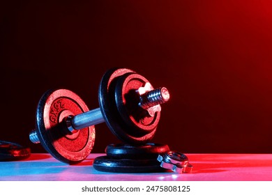 Barbell and parts of one on table in color lights. Space for text