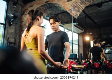 Barbell weight training , Asian man trainer coach helping woman bicep exercise with barbell in fitness gym. Healthy lifestyle young female workout training lifting dumbbell with professional trainer.