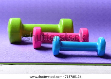 Barbells in different colors placed in pattern, close up. Sports and healthy lifestyle concept. Shaping and fitness equipment. Dumbbells made of pink, green and cyan plastic on purple background