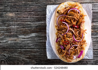 Barbeque Pulled Pork ciabatta open Sandwich with BBQ Sauce, red onion and chili pepper on parchment paper on oval plate, copyspace left, view from above