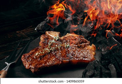 barbeque steak on a black slate board with meat fork and grill coals next to it