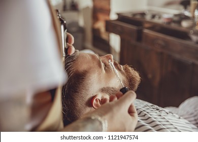 The barber applies the beard oil with a dropper. Photo in vintage style
