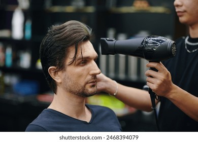 Barber blow drying wet hair of man visiting beauty salon - Powered by Shutterstock