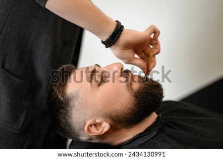 Barber combs beard with comb while cutting and shaving Caucasian man