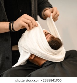 The barber covers the clients face with a hot wet towel to steam off the beard. - Powered by Shutterstock