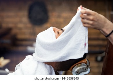 Barber covers the face of a man with a hot towel. Traditional ritual of shaving the beard with hot and cold compresses in a old style barber shop. Hot towel on face before shaving in barber shop - Powered by Shutterstock