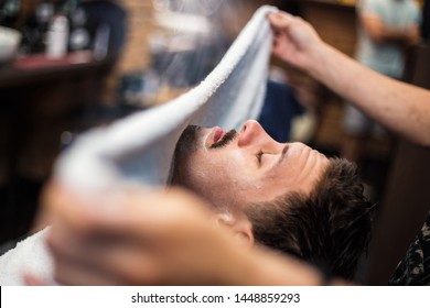 Barber covers the face of a man with a hot towel. Traditional ritual of shaving the beard with hot and cold compresses in a old style barber shop. Hot towel on face before shaving in barber shop - Powered by Shutterstock