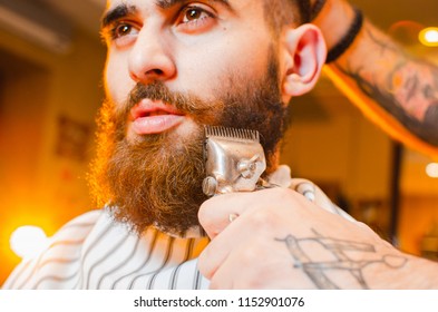 Barber Cuts A Beard Of Vintage Hair Clippers To A Young Handsome Guy With A Beard And Mustache. Men's Hair Salon.