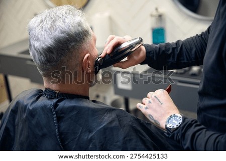 Barber cutting and styling the beard of a gray-haired man