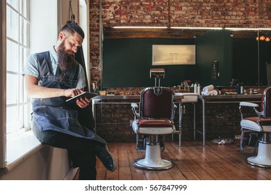 Barber with digital tablet sitting on window sill of salon. Hairdresser organizing his business using latest technology. - Powered by Shutterstock