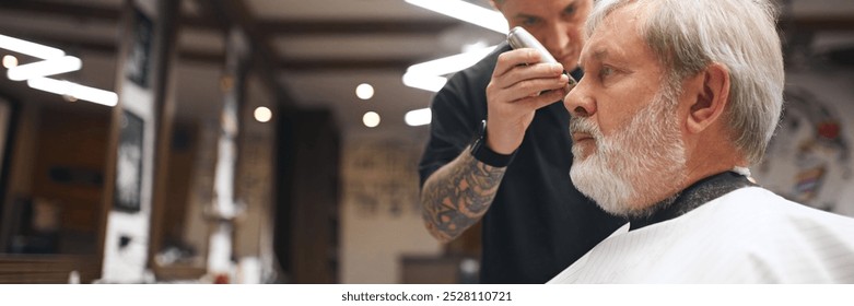 Barber, with focused attention, trimming client beard and mustache, ensuring clean lines. Elderly man visiting barbershop. Banner. Concept of male beauty, barbershop, hairstyle, salon, hairdresser - Powered by Shutterstock