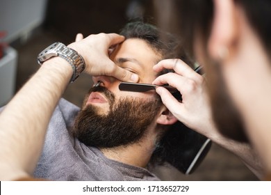 
Barber hands with a razor shaving beard of male customer