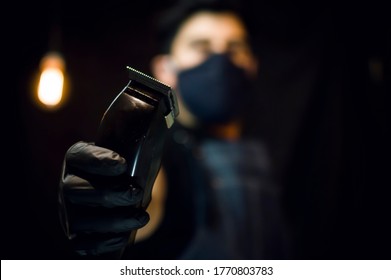 Barber Holding A Black Hair Clipper Wearing A Black Face Mask On Dark Background