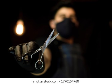 Barber Holding Scissors With One Hand On Dark Background Wearing A Face Mask