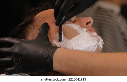 Barber Man Is Shaving Client With A Vintage Straight Razor In A Barbershop. Shaving Cream, Foam. Classic Shave By Stainless Steel Straight Edge Razor