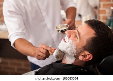 Barber Putting Some Shaving Cream On A Client Before Shaving His Beard In A Barber Shop