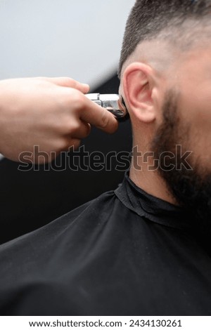 Similar – Image, Stock Photo Barber shaves the temple with cordless trimmer during a short haircut on the sides of the head.