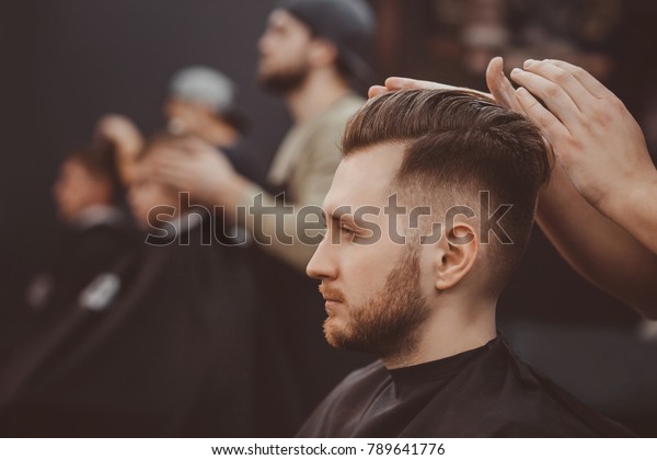 Barber shop. Man in barber\'s chair, hairdresser\
styling his hair