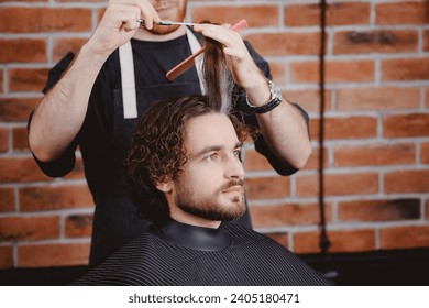 Barber shop, warm toning photo. Man in barbershop chair, hairdresser styling his long hair. - Powered by Shutterstock