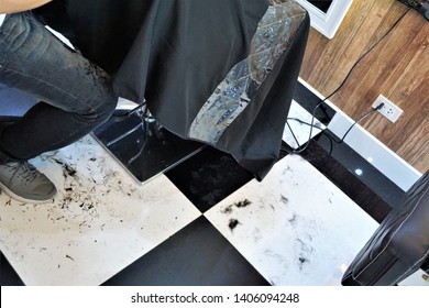 In The Barber Shop Where The Hairdresser Is Cutting The Hair For The Client And The Hair Falls On The Black And White Tile Floor.