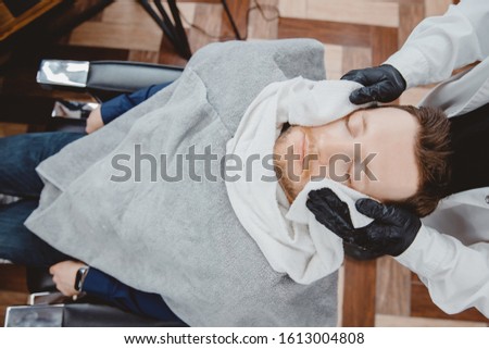 Barber steam face skin of man with hot towel before royal shave in Barbershop.