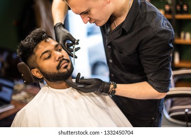 Barber styling beard with scissors at barbershop. Stylish hairdresser in man hair salon