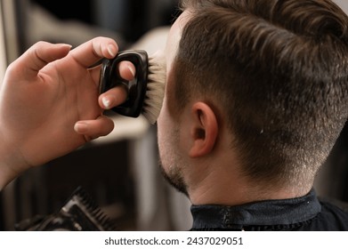 A barber sweeps hair with a brush while trimming customers beards with an electric trimmer in the salon. - Powered by Shutterstock