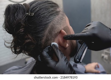 A barber uses an alcohol soaked cotton ball to moisturize and clean the back of a customer's ear before shaving. - Shutterstock ID 2184978193