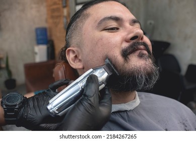 A Barber Uses A Cordless Trimmer To Shave Off The Beard Of A Customer Going For A Clean Shaven Face And New Look.